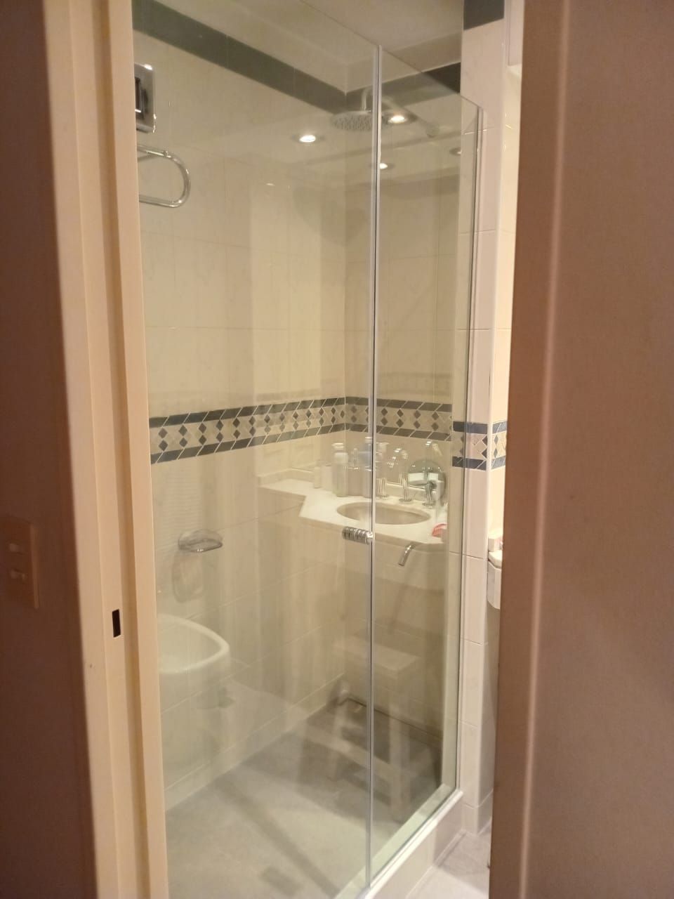 Mampara de ducha de cristal en baño con azulejos blancos y azules y lavabo.