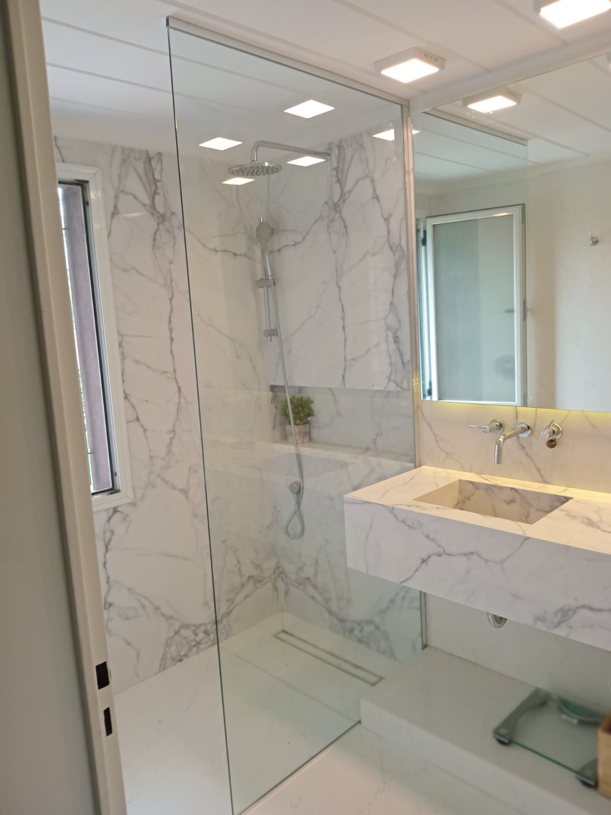 Baño con azulejos efecto mármol, mampara de ducha de cristal y lavabo rectangular.