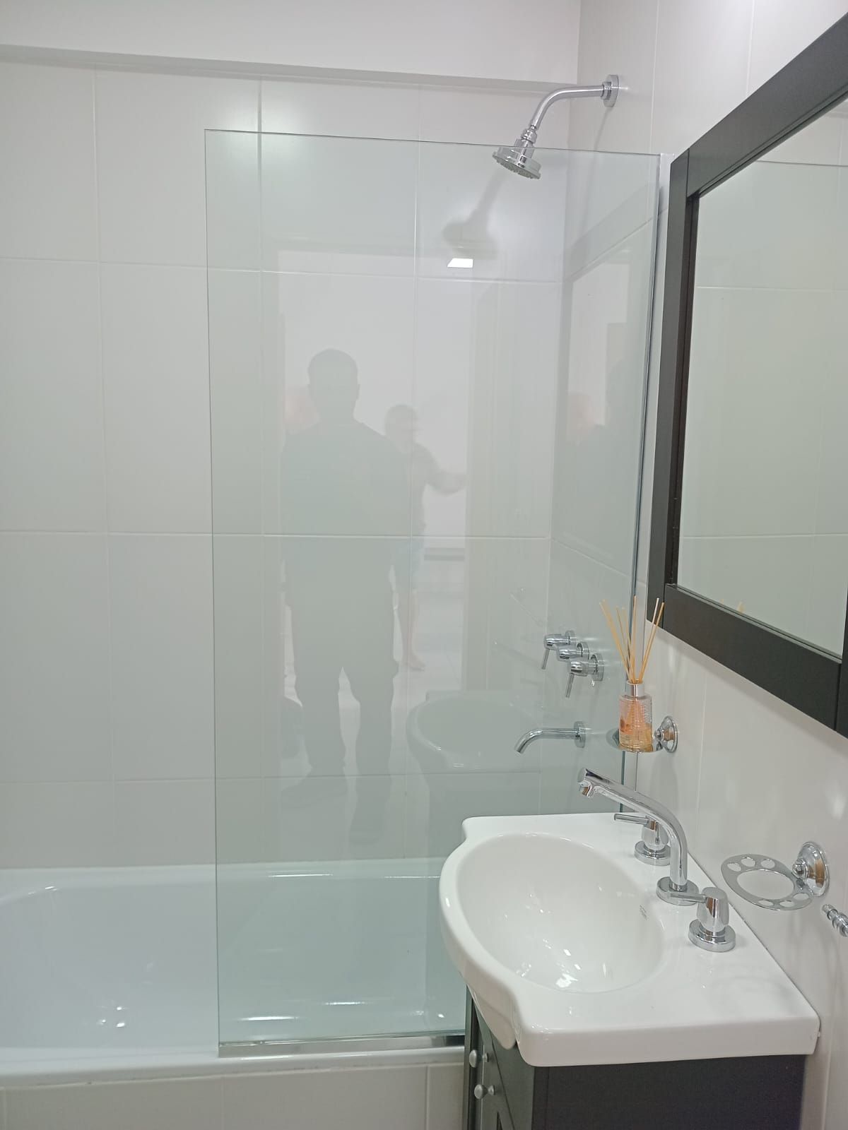 Baño con bañera blanca, mampara de cristal, lavabo y espejo.
