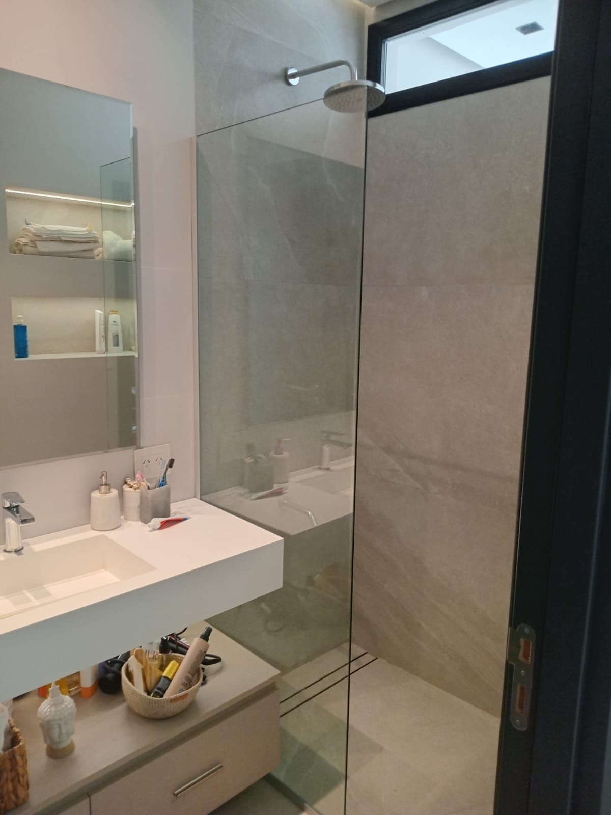 Baño moderno con ducha de cristal, tocador y grandes paredes de azulejos.