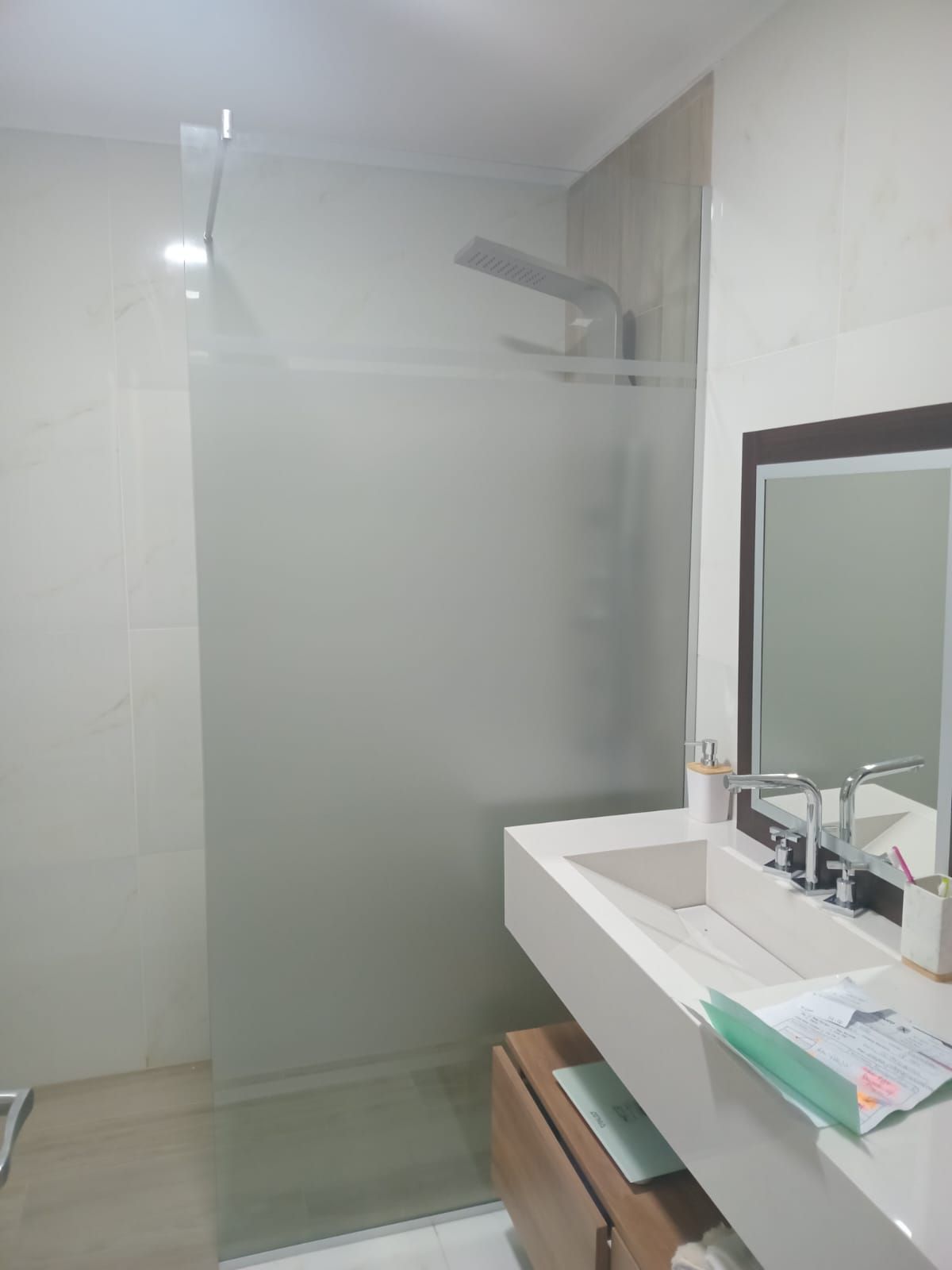 Baño moderno con ducha de cristal esmerilado, lavabo blanco y espejo grande.