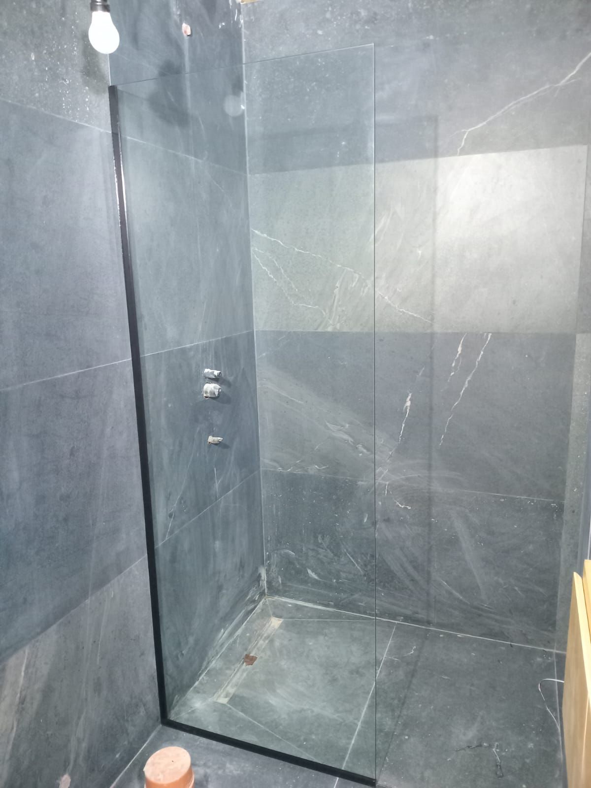 Cabina de ducha con azulejos grises y puerta de cristal. Grifería cromada.