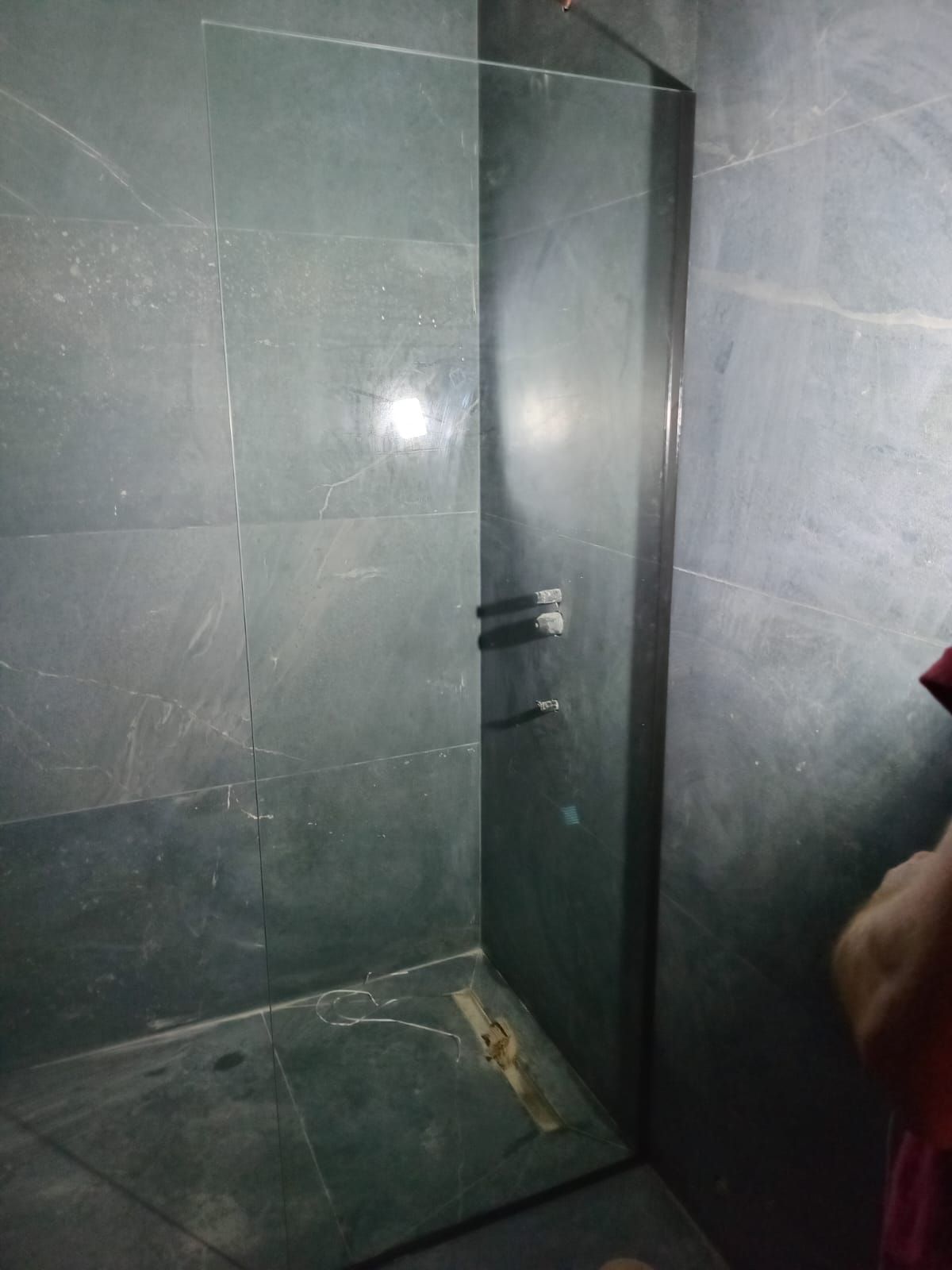 Una mampara de ducha de cristal en un baño con azulejos de color gris oscuro.