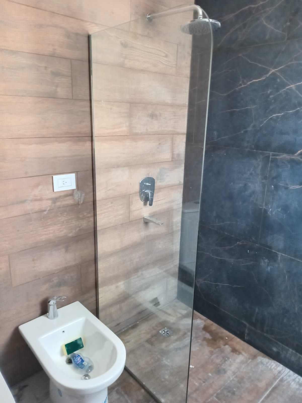 Mampara de ducha con mampara de cristal, paredes de azulejos y bidet.