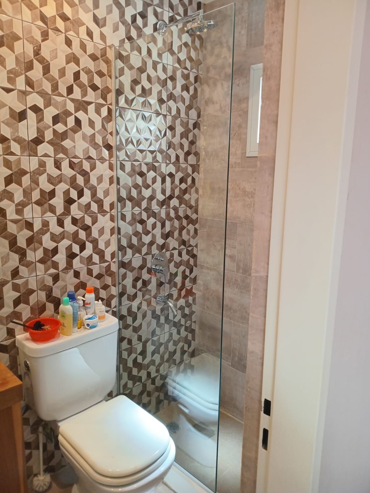 Baño con paredes de azulejos estampados, puerta de ducha de vidrio y un inodoro blanco.
