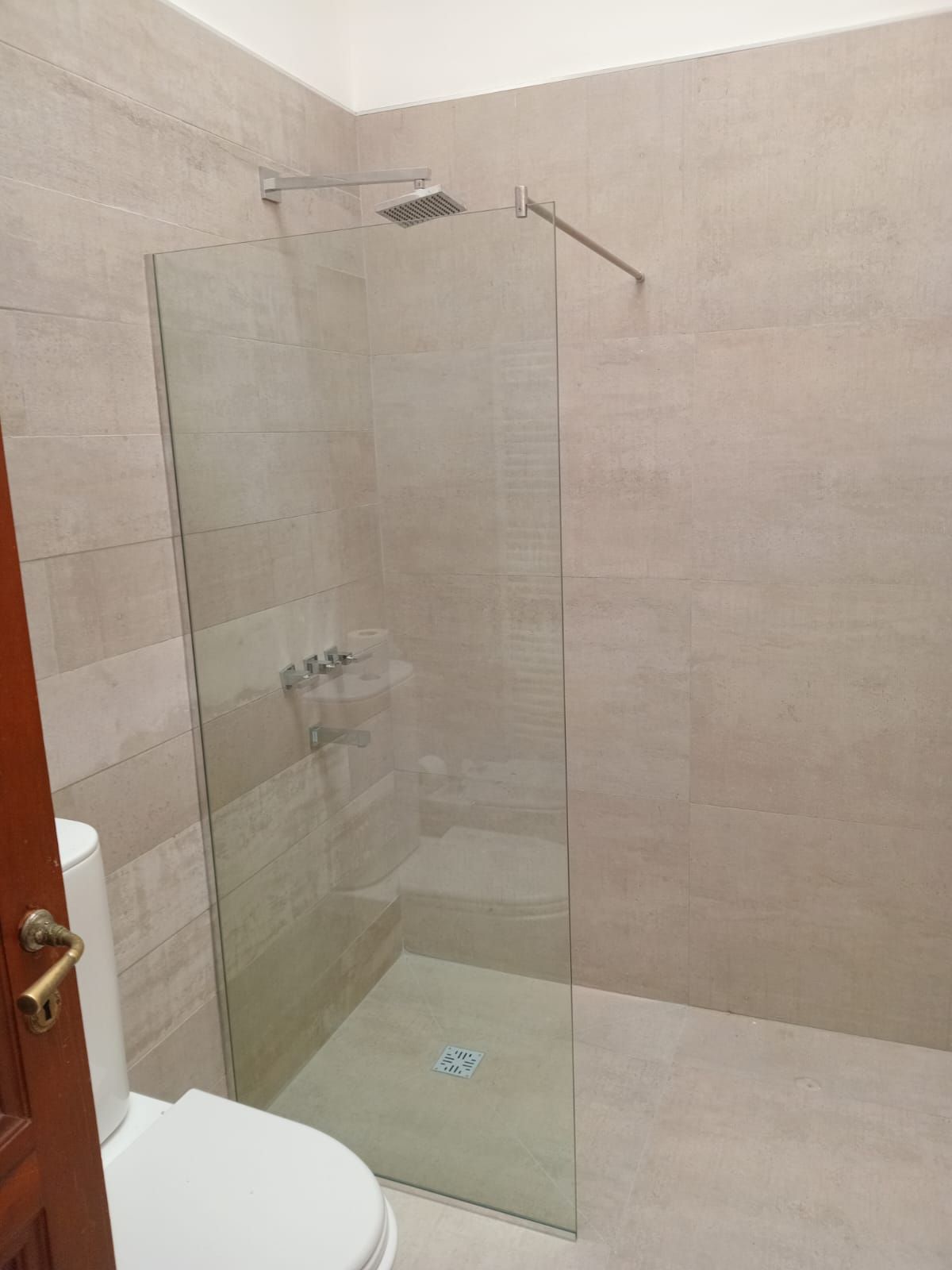 Baño con mampara de ducha de cristal, inodoro y paredes de azulejos beige.