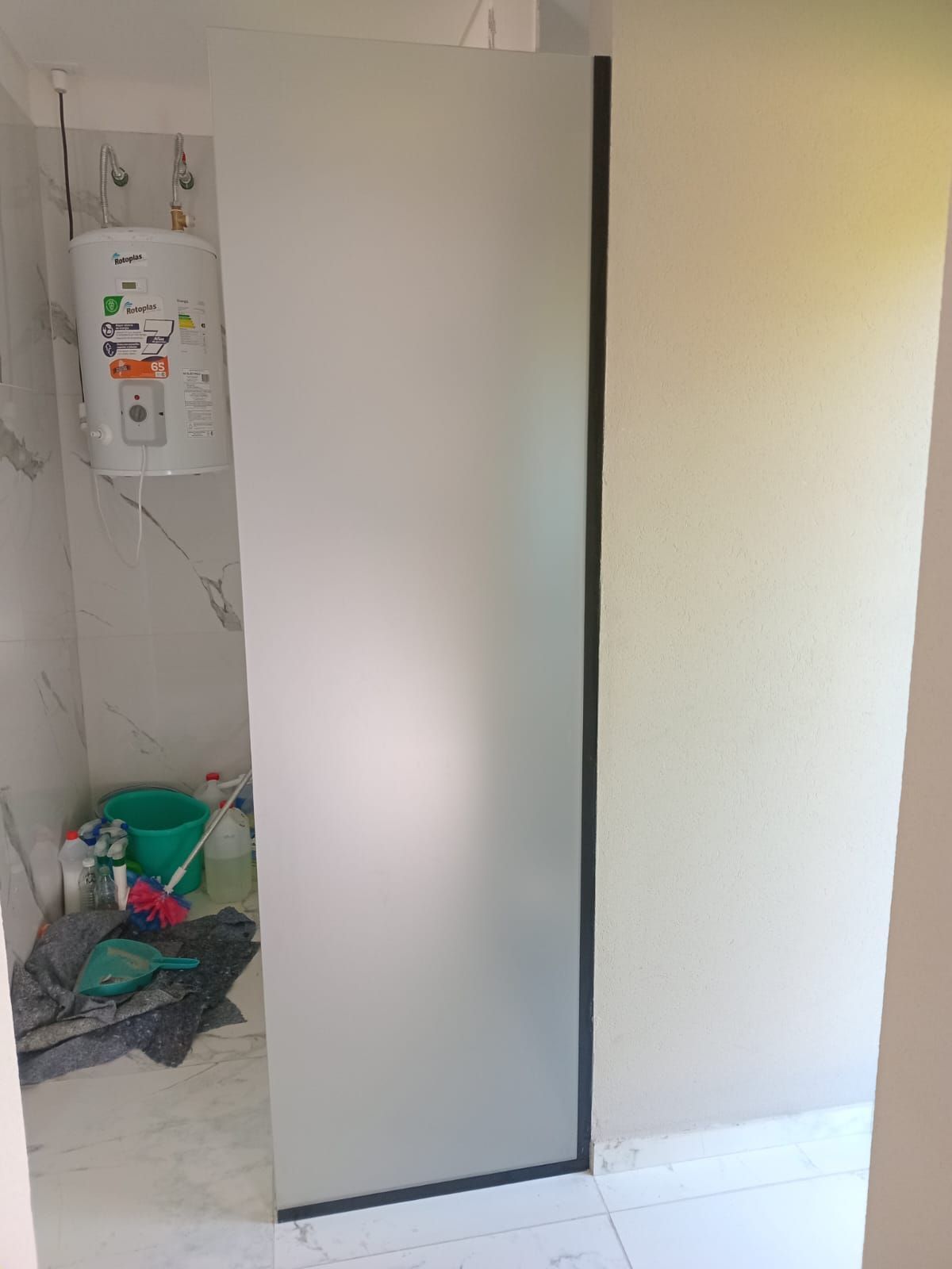 Puerta de ducha de vidrio esmerilado en un baño, calentador de agua en la pared.