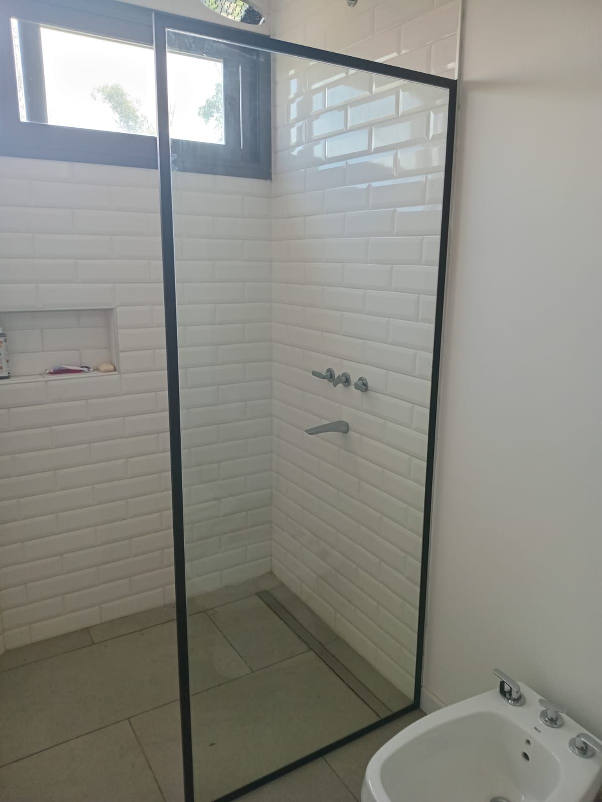 Cabina de ducha con marco negro y azulejos de ladrillo blanco.