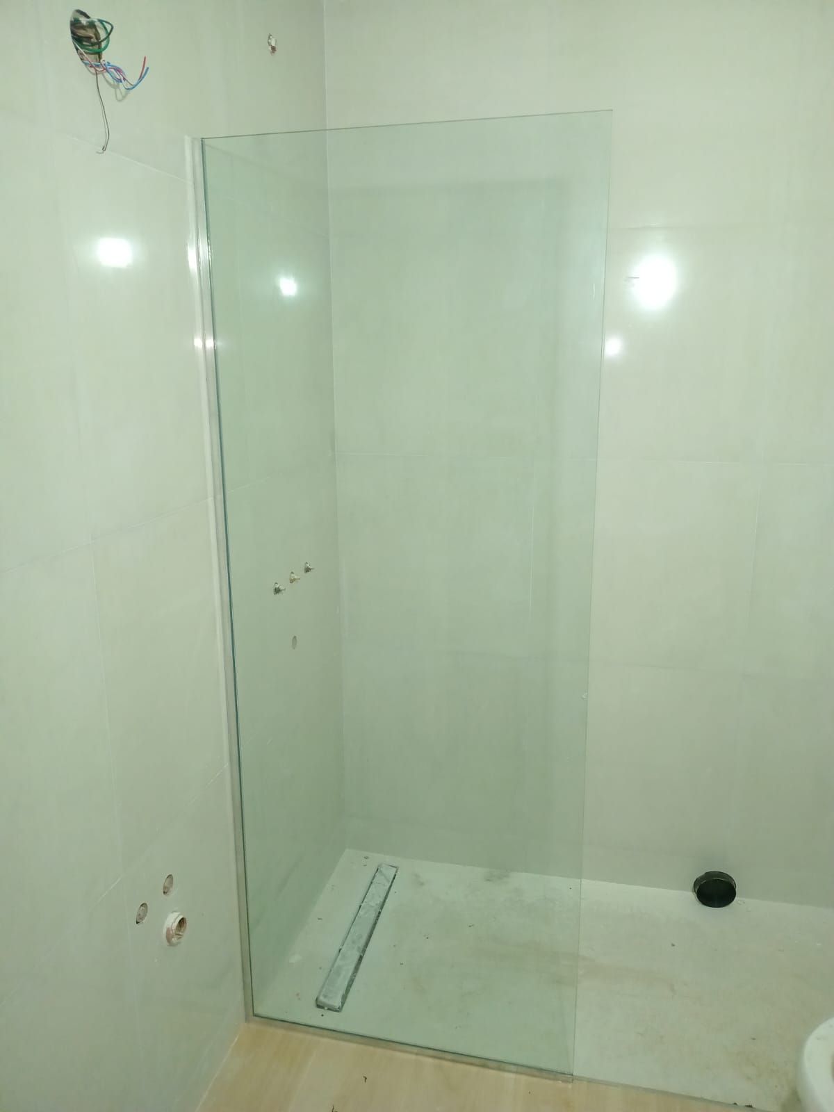 Mampara de ducha de cristal en un baño alicatado. Se ve un desagüe lineal en el suelo.