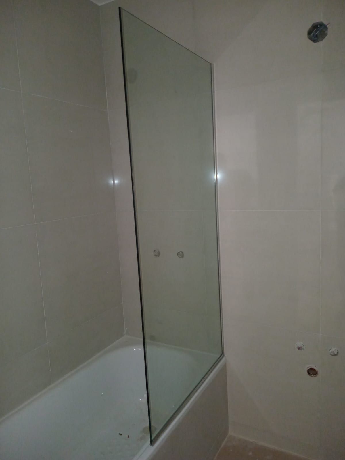 Mampara de ducha de cristal transparente sobre una bañera blanca. Las paredes son de color beige claro.