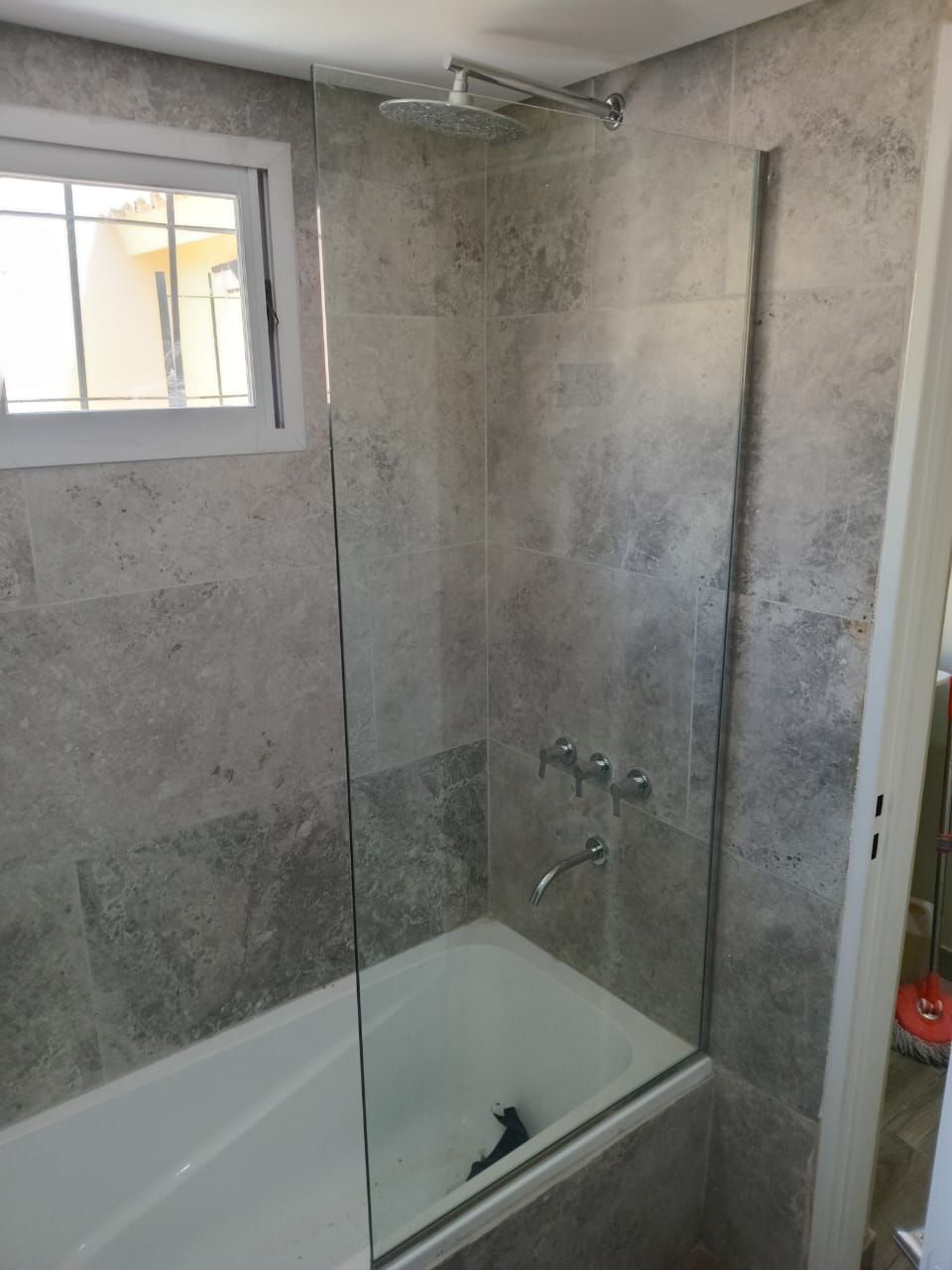 Zona de ducha con paredes revestidas de azulejos grises, bañera y mampara de cristal.