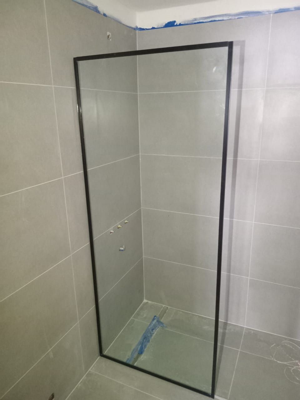 Mampara de ducha de cristal con marco, instalada en un baño alicatado. El marco es negro.