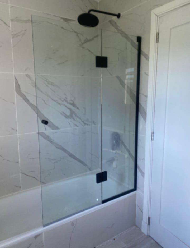 Una mampara de ducha de vidrio con marco negro instalada en una bañera, frente a azulejos