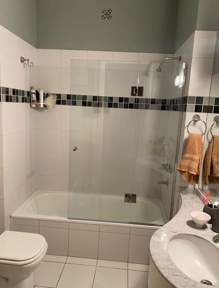 Baño con azulejos blancos, bañera, puerta de ducha de cristal y encimera gris con lavabo.