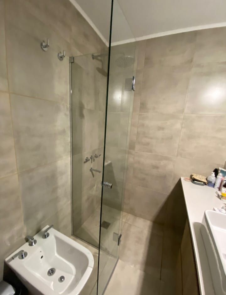 Baño con mampara de ducha de cristal, paredes alicatadas, bidé y lavabo sobre encimera.