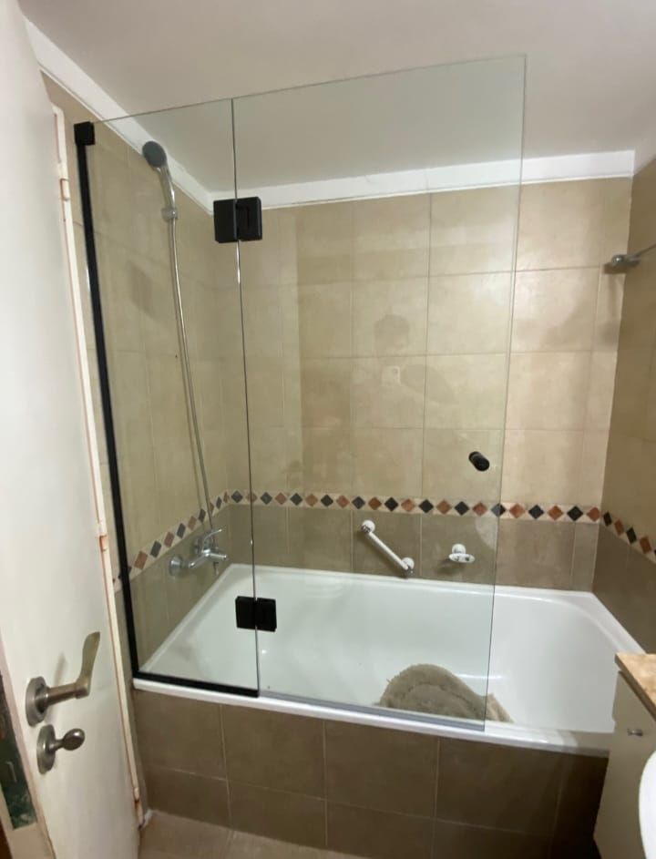 Baño con bañera y mampara de ducha de cristal transparente. Paredes de azulejos beige y grifería cromada.