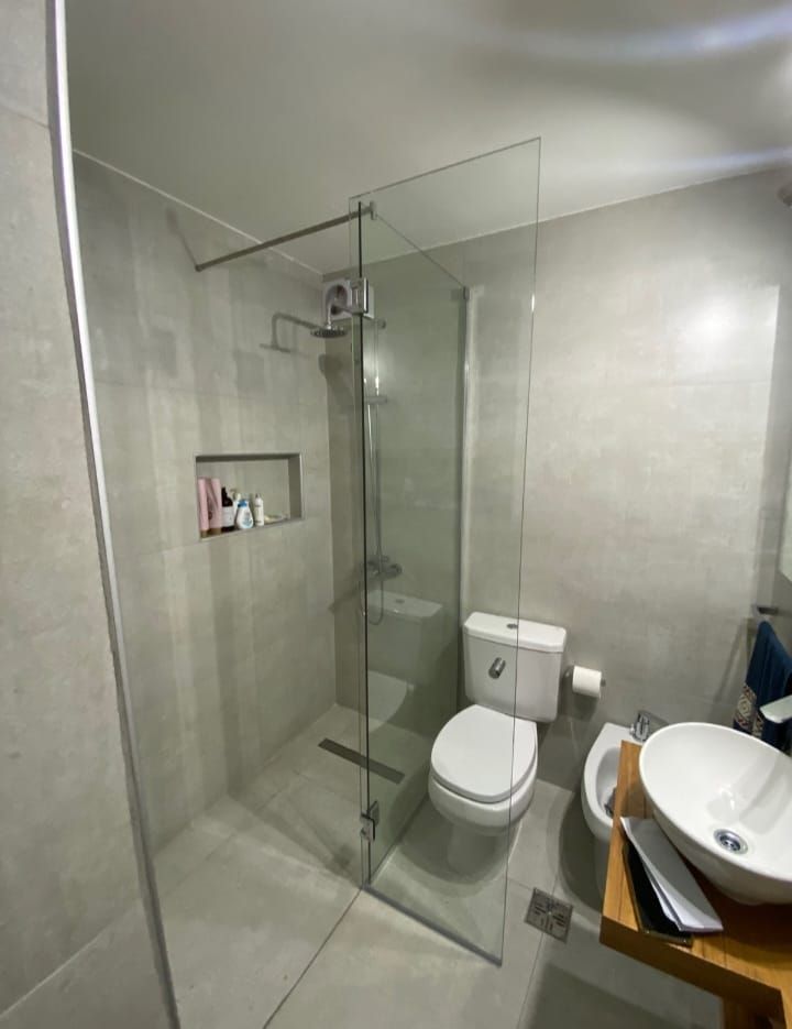 Baño moderno con ducha de cristal, inodoro y lavabo sobre encimera. Paredes de azulejos grises.