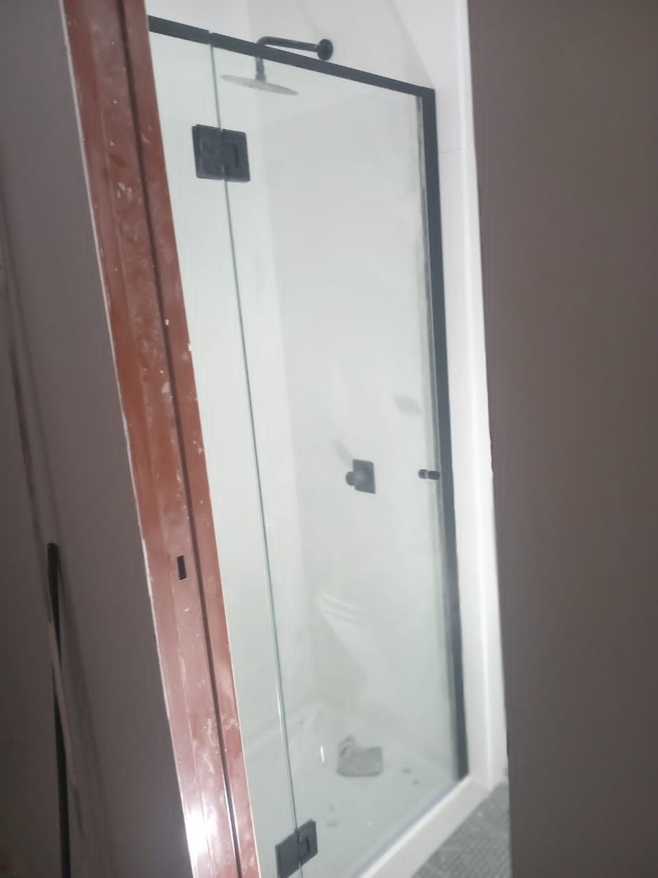 Puerta de ducha de vidrio con marco y herrajes negros, instalada en un baño blanco.