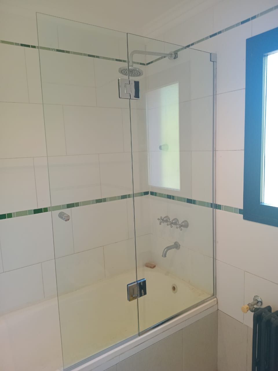 Mampara de ducha de vidrio transparente sobre una bañera blanca con paredes de azulejos blancos