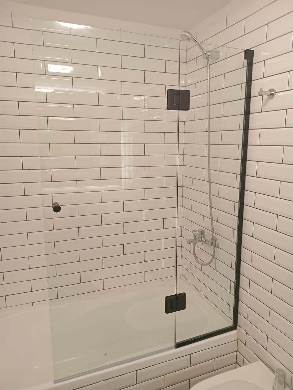 Ducha con puerta de cristal, marco y bisagras de color negro, azulejo tipo metro de color blanco.