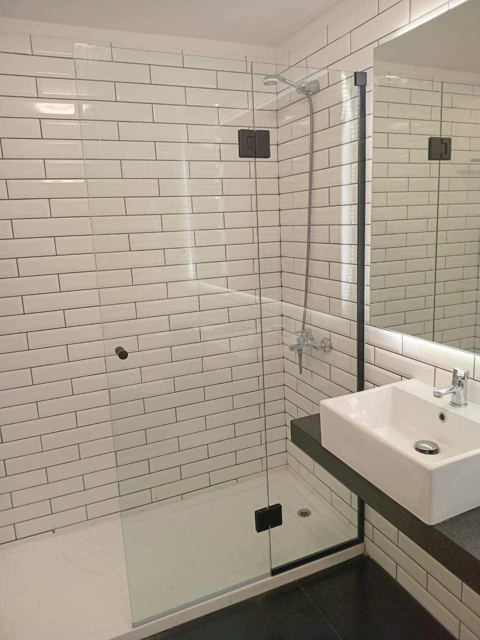 Baño moderno con ducha con azulejos blancos tipo metro, puerta de cristal, lavabo rectangular y espejo grande.