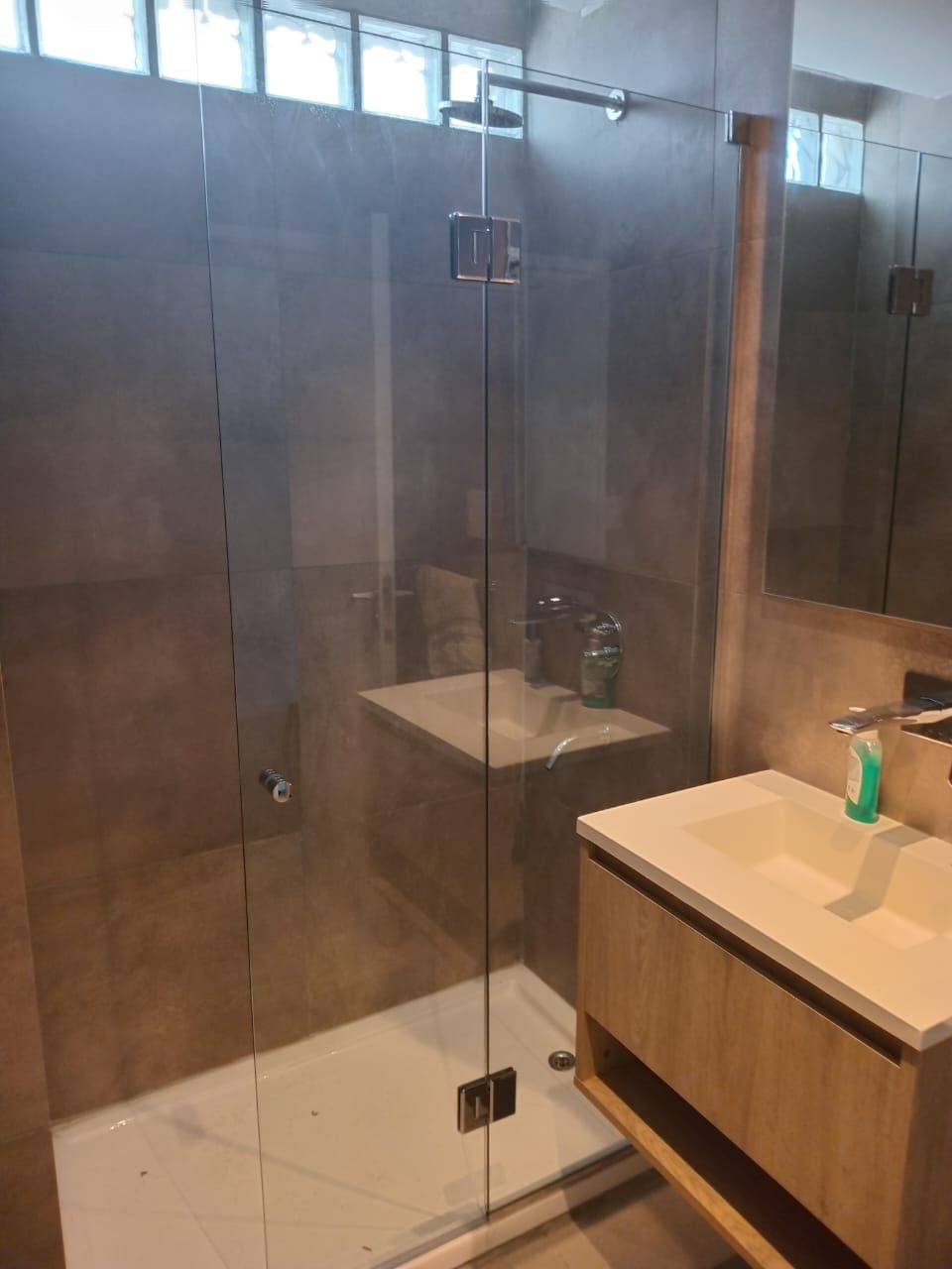 Baño con ducha de cristal, tocador de madera y lavabo blanco.