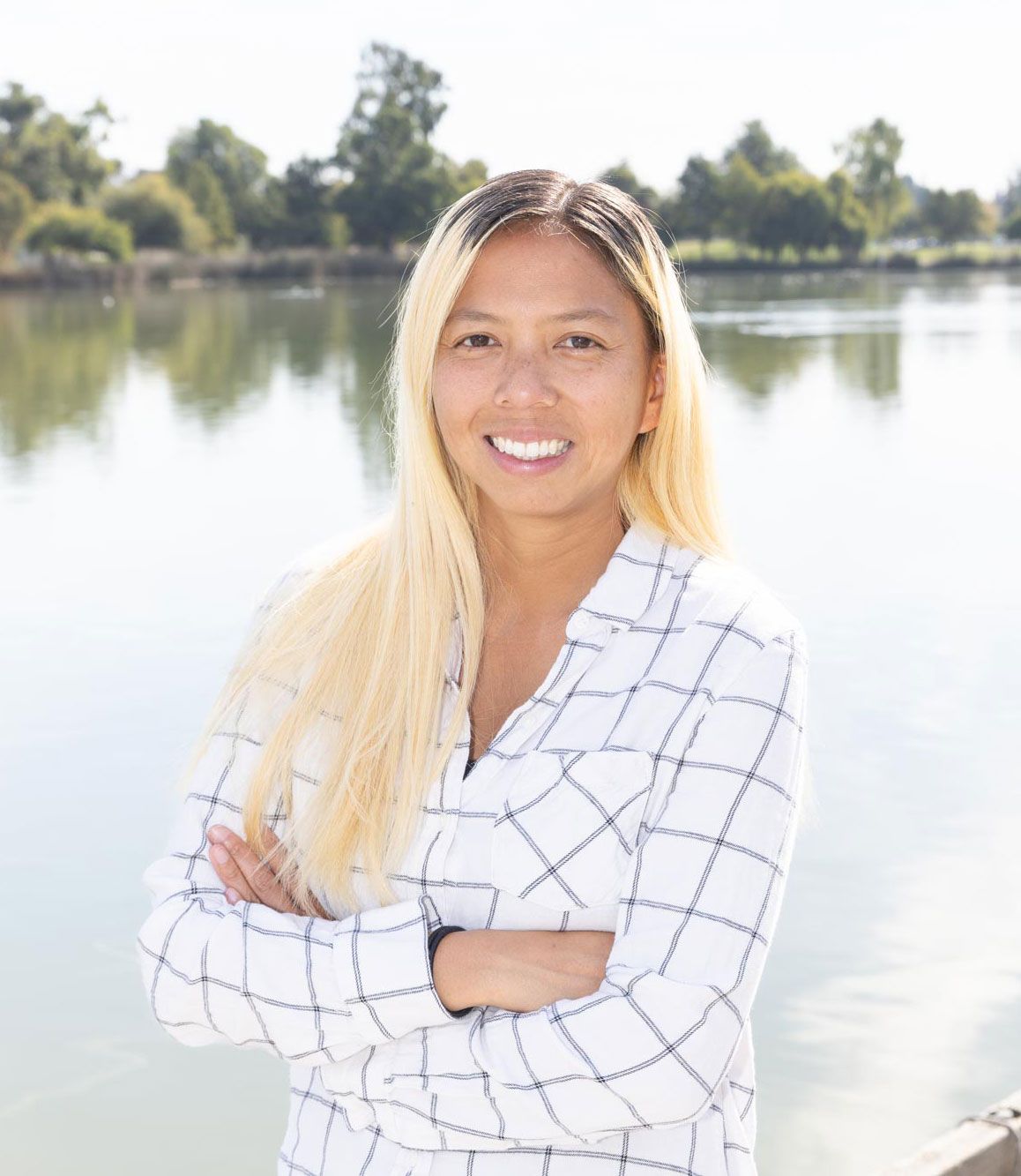A woman is standing in front of a lake with her arms crossed.