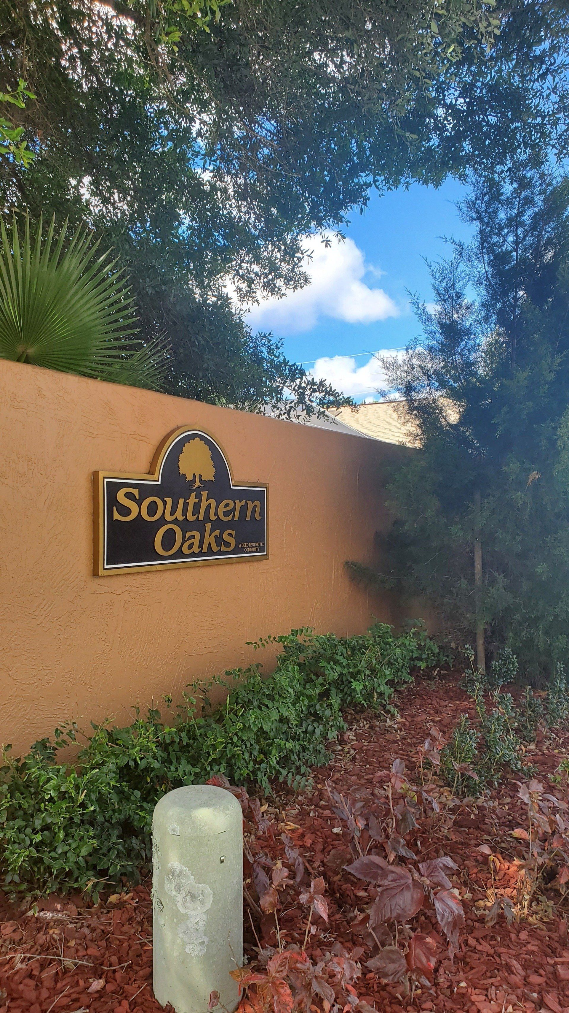 A sign for southern oaks is on a wall next to a tree.