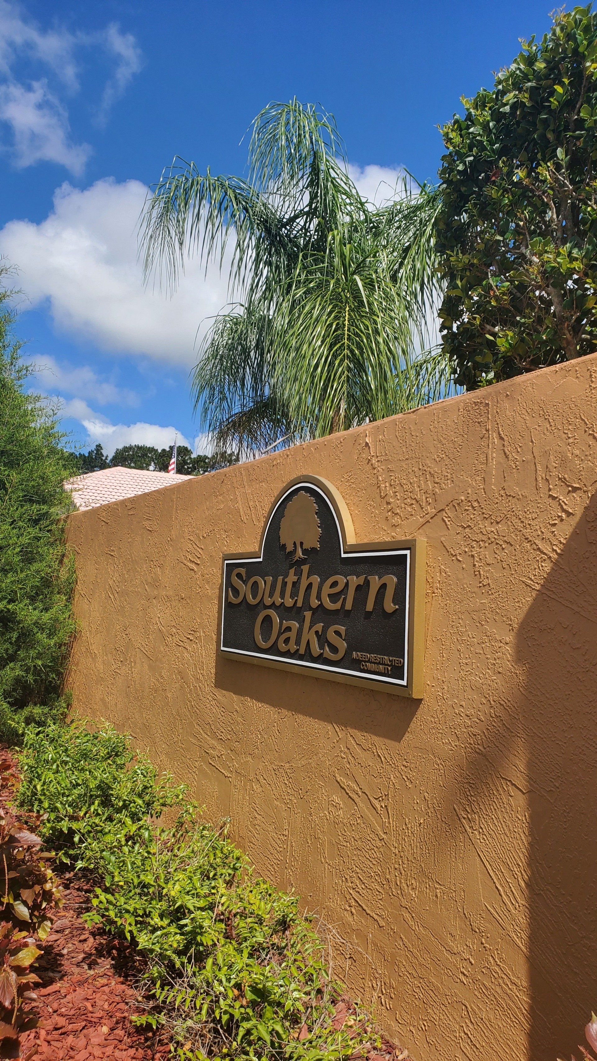 A sign on a wall that says `` southern oaks '' is surrounded by trees and bushes.