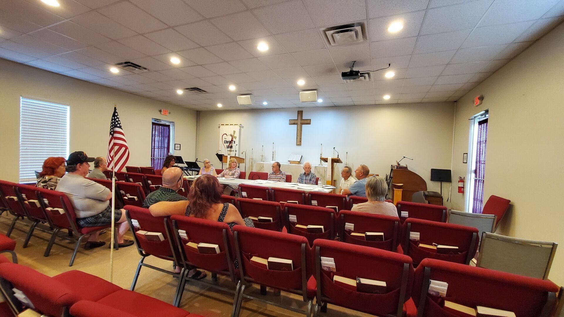 A group of people are sitting in rows of red chairs in a church.