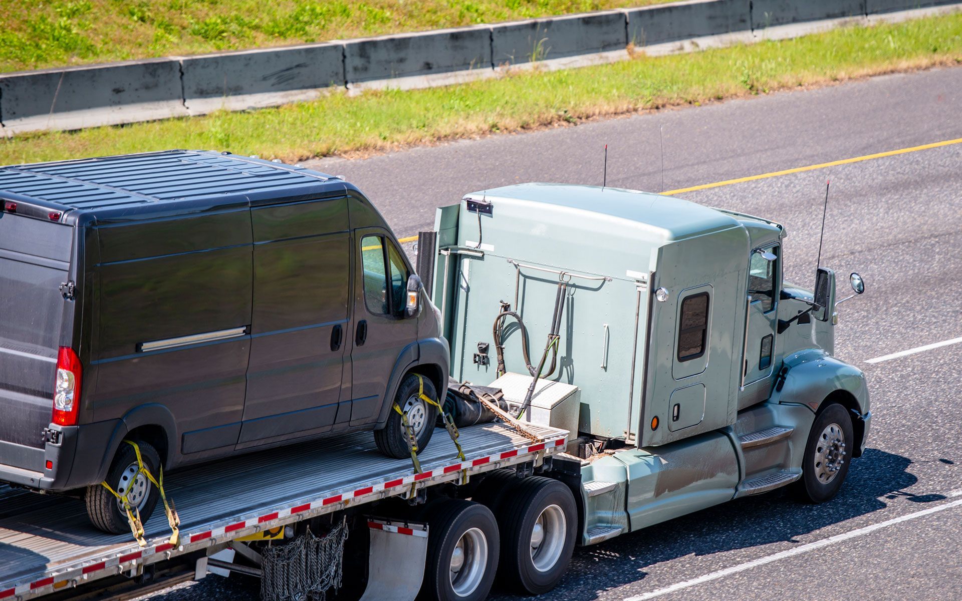 A semi truck is towing a van down a highway.