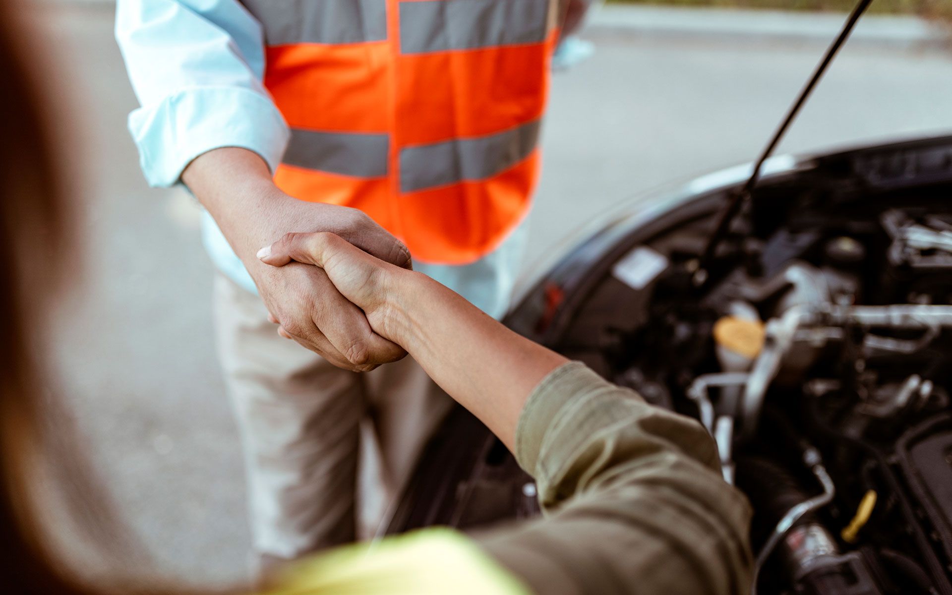 A man is shaking hands with a woman in front of a broken down car.