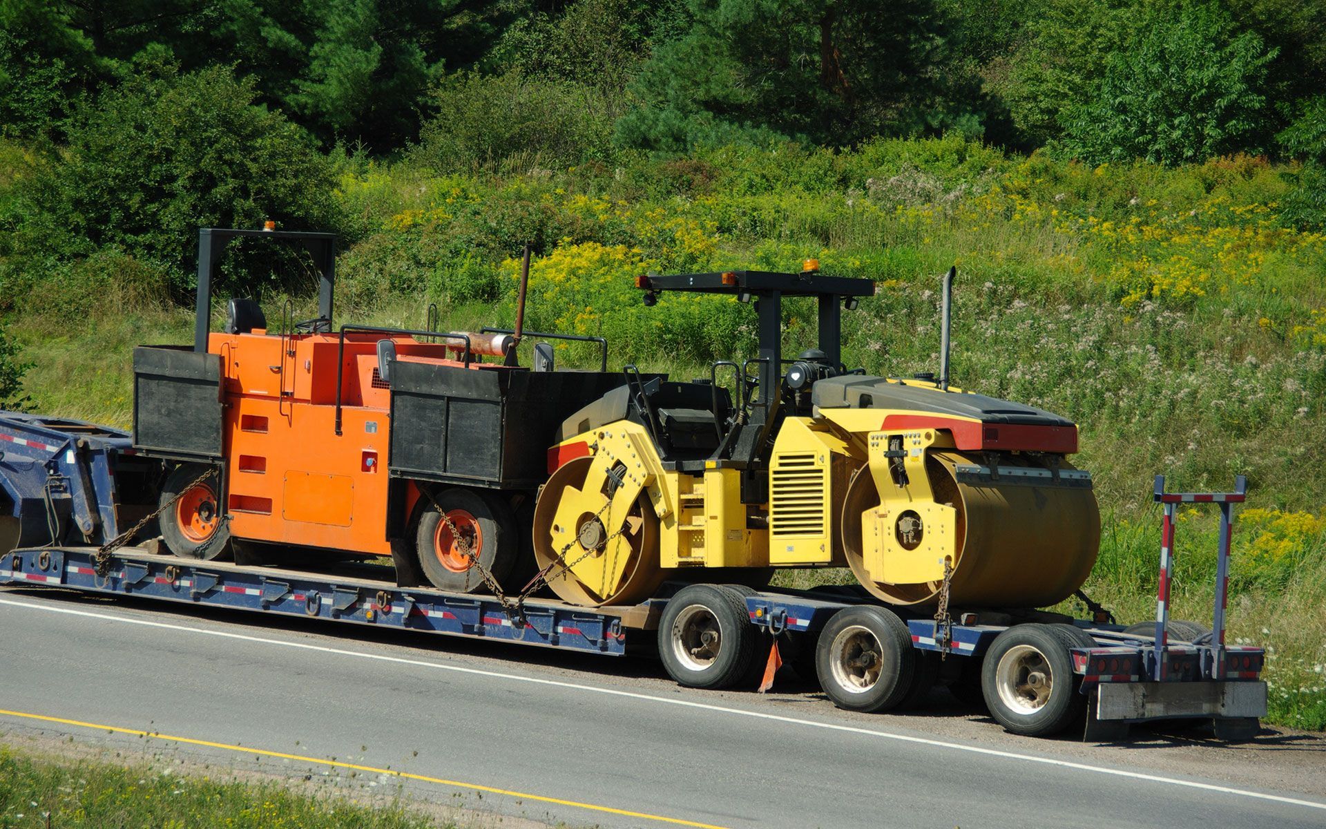 A tractor is being transported on a trailer on a highway