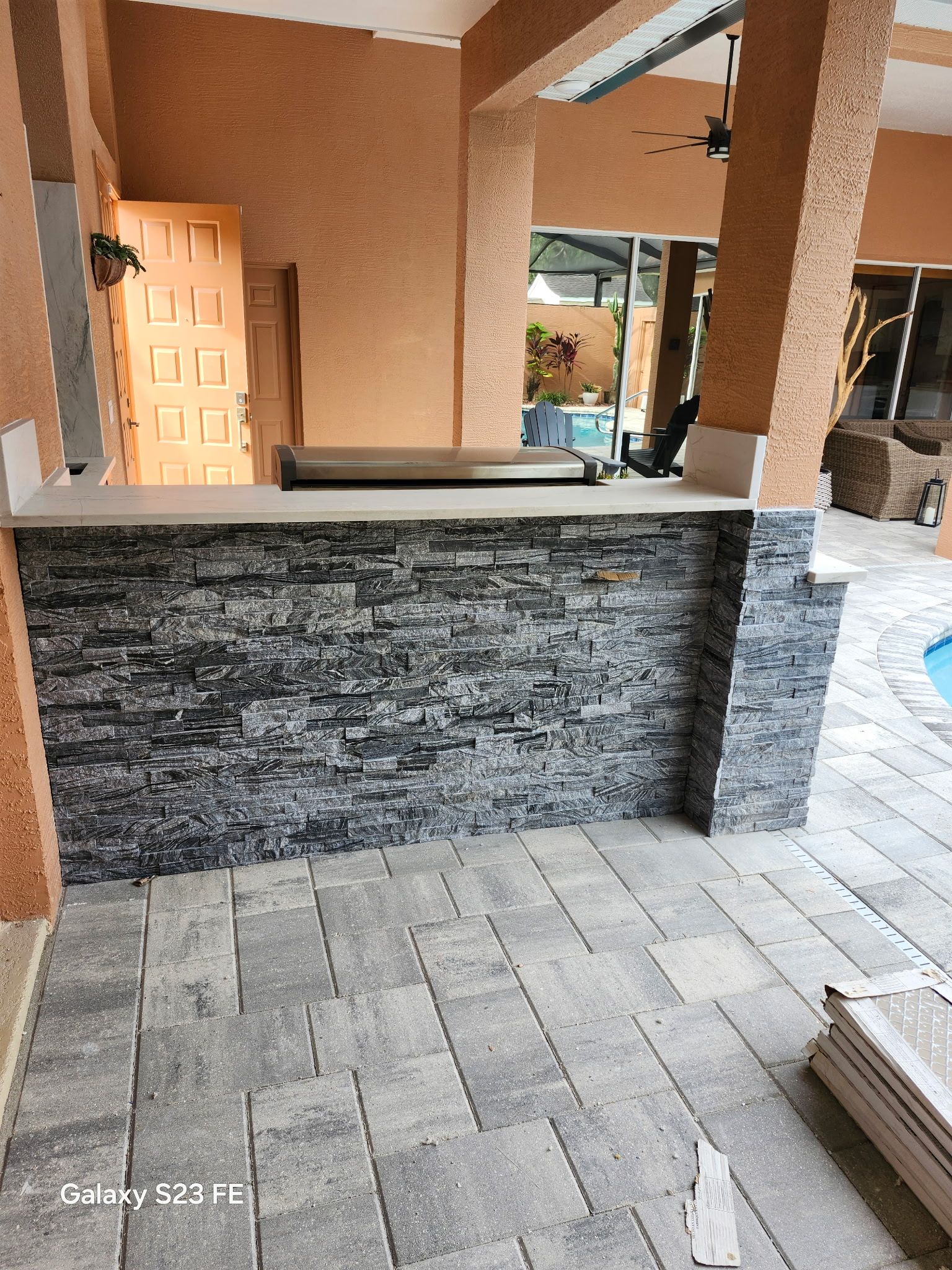Outdoor bar with gray stone facade, concrete pavers, and a pool visible in the background.