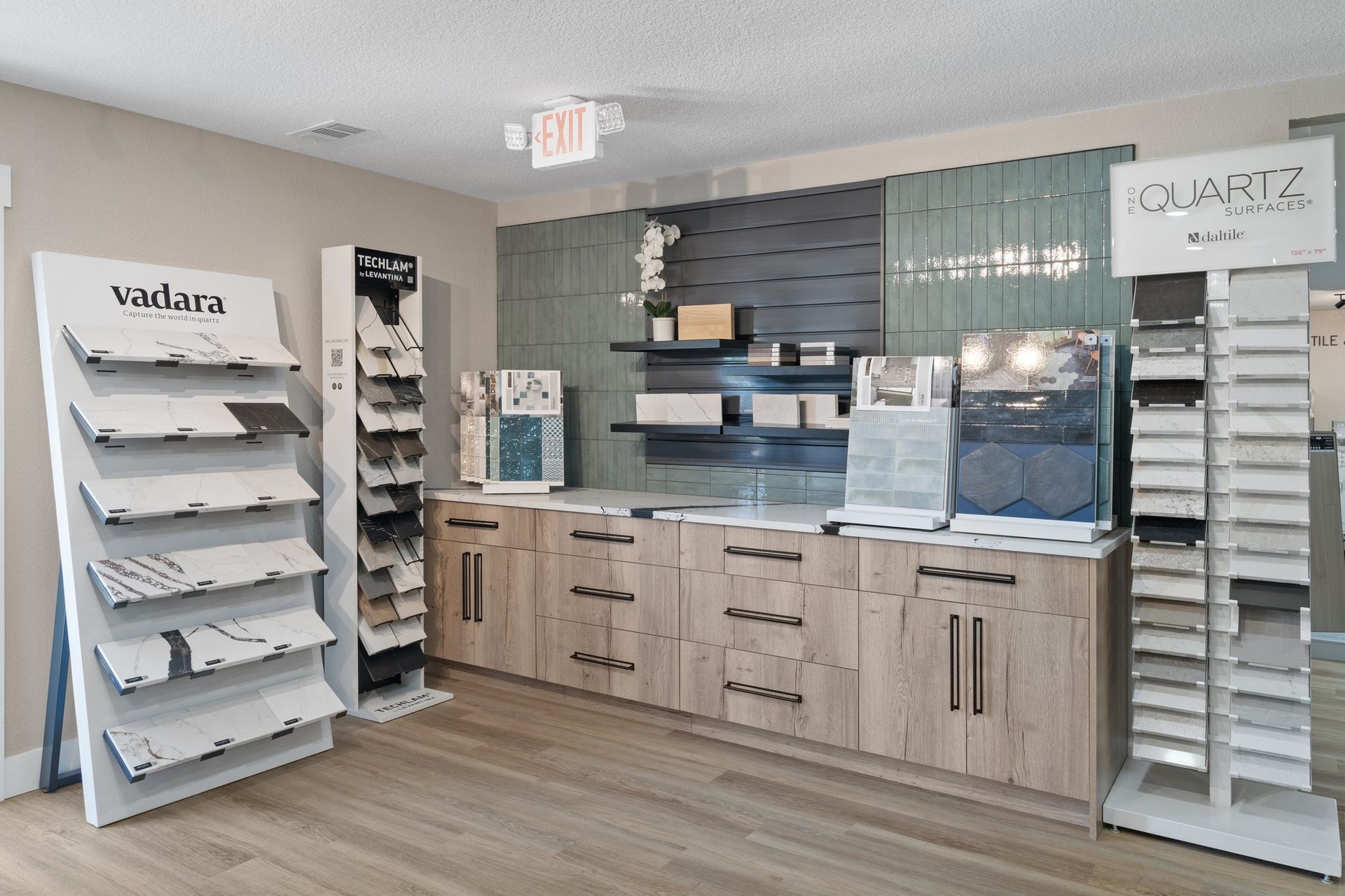 Tile and countertop showroom displays quartz and marble samples on light wood cabinetry.