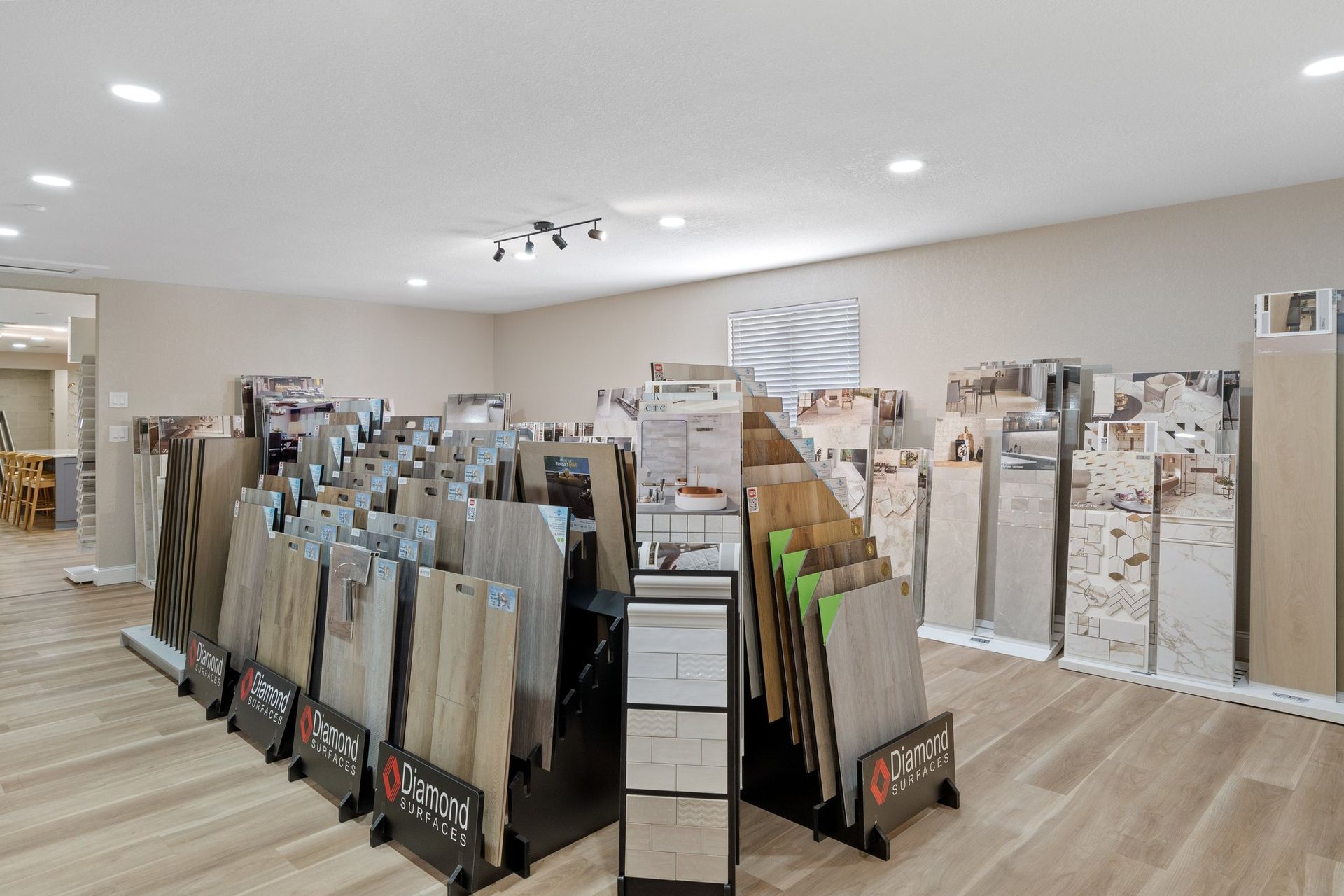 Tile showroom with displays of various tiles on stands, light-colored walls and flooring.