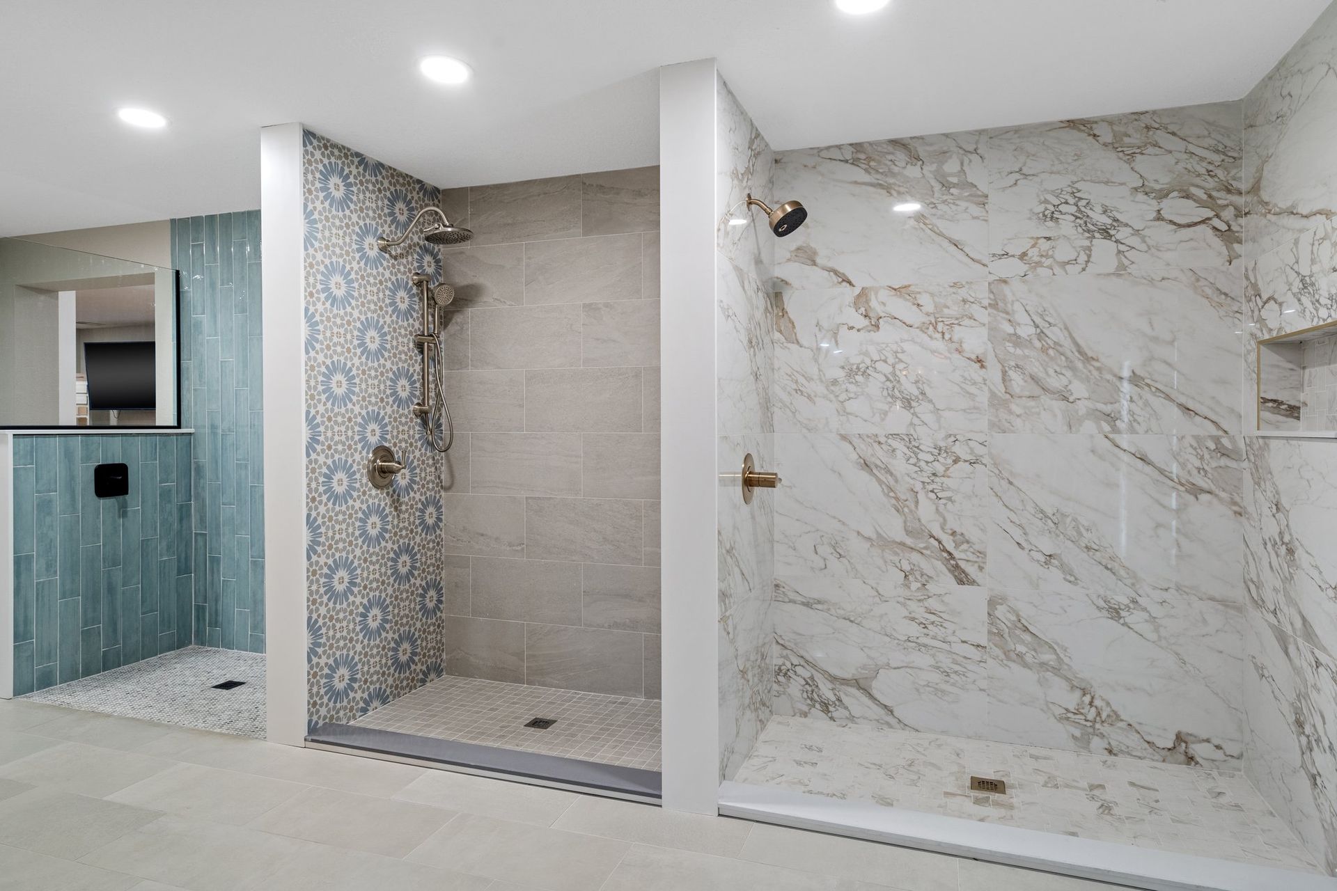 Three modern shower stalls with different tile designs and fixtures, lit by recessed ceiling lights.