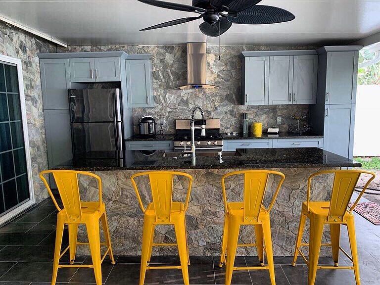 Outdoor kitchen with gray cabinets, stainless steel appliances, black countertop, and yellow bar stools.