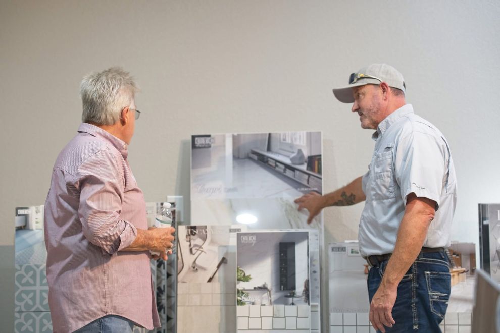 Two men looking at tile samples, one pointing. Neutral-toned room.