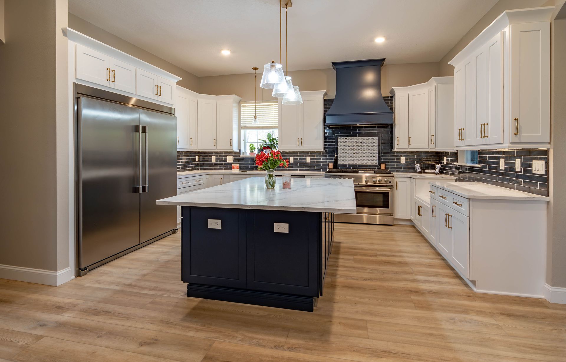 Modern kitchen with white cabinets, navy island and range hood, stainless steel appliances, and light wood floors.
