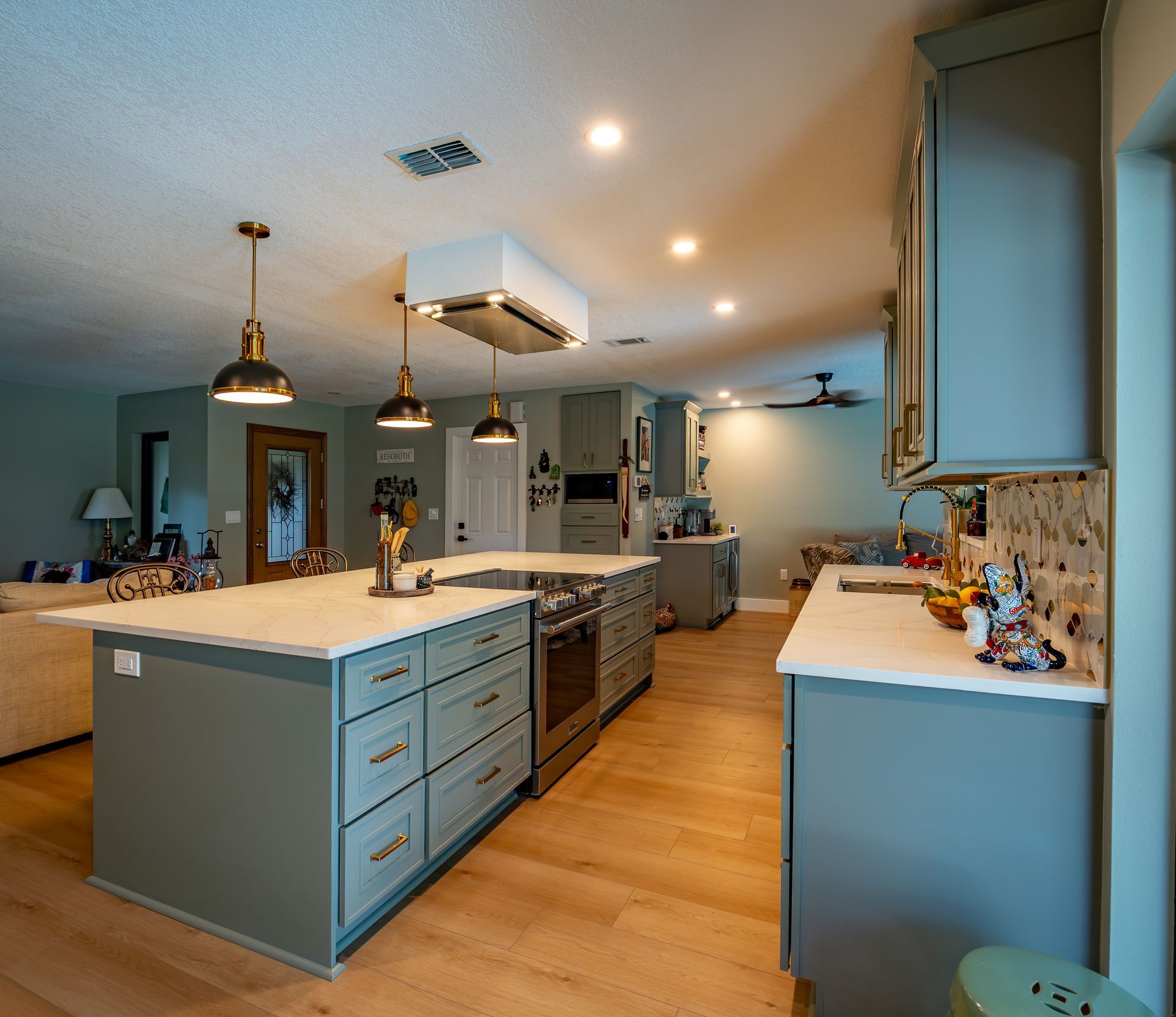 Spacious kitchen with blue cabinets, white countertops, and wooden floors. Island with cooktop and pendant lights.