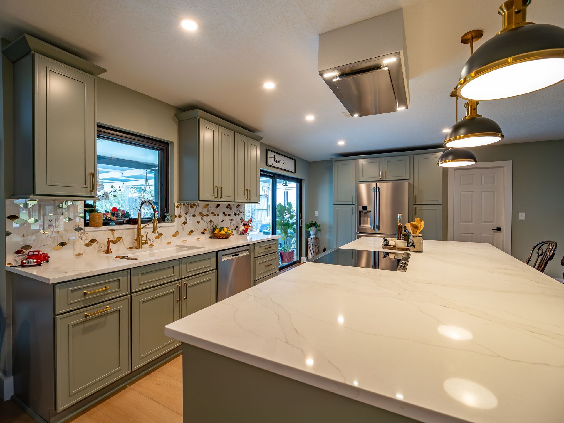 Modern kitchen with green cabinets, marble countertops, and stainless steel appliances.