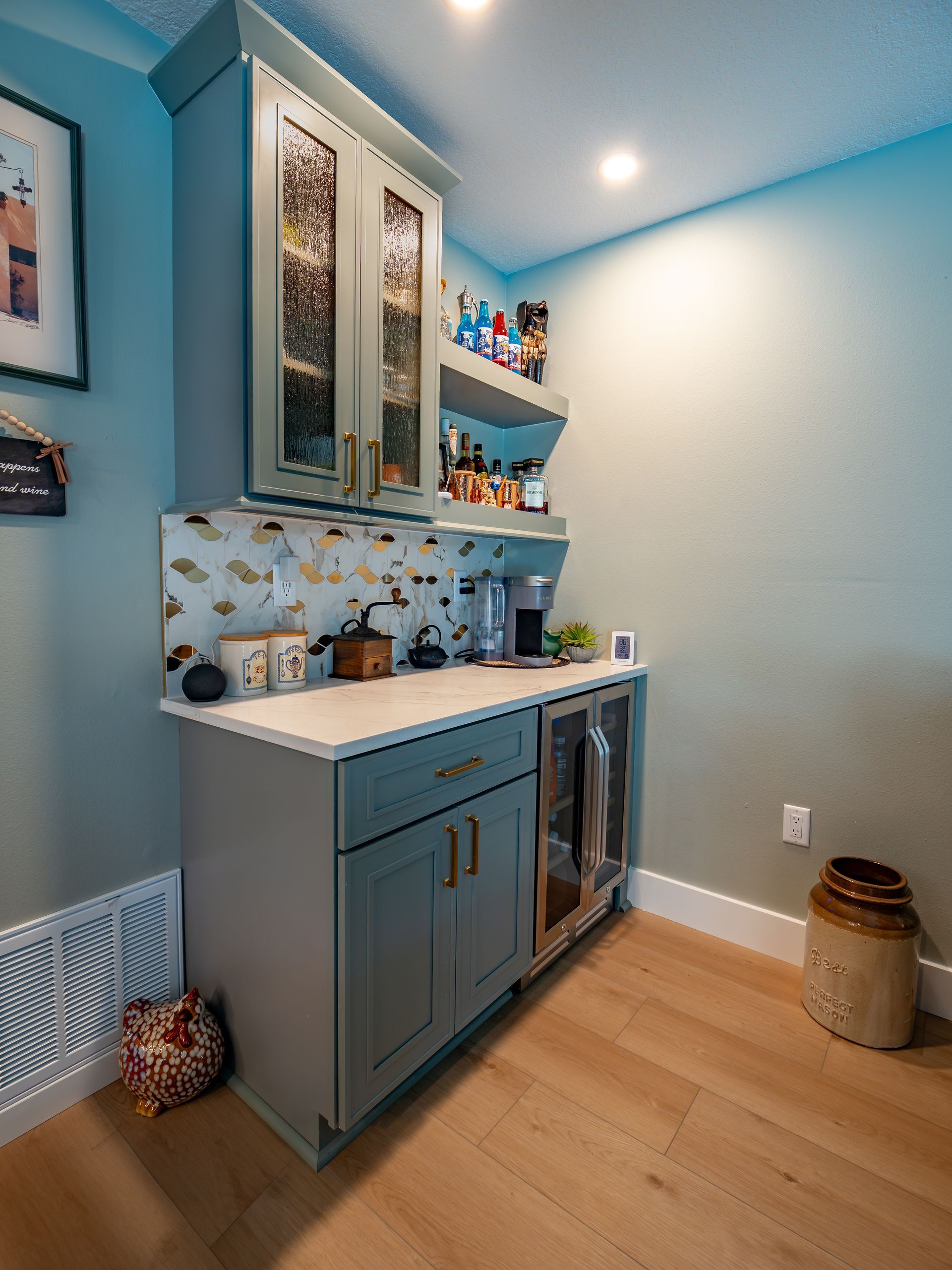 A teal built-in coffee bar with cabinets, shelves, and a small refrigerator. Includes countertop and gold hardware.