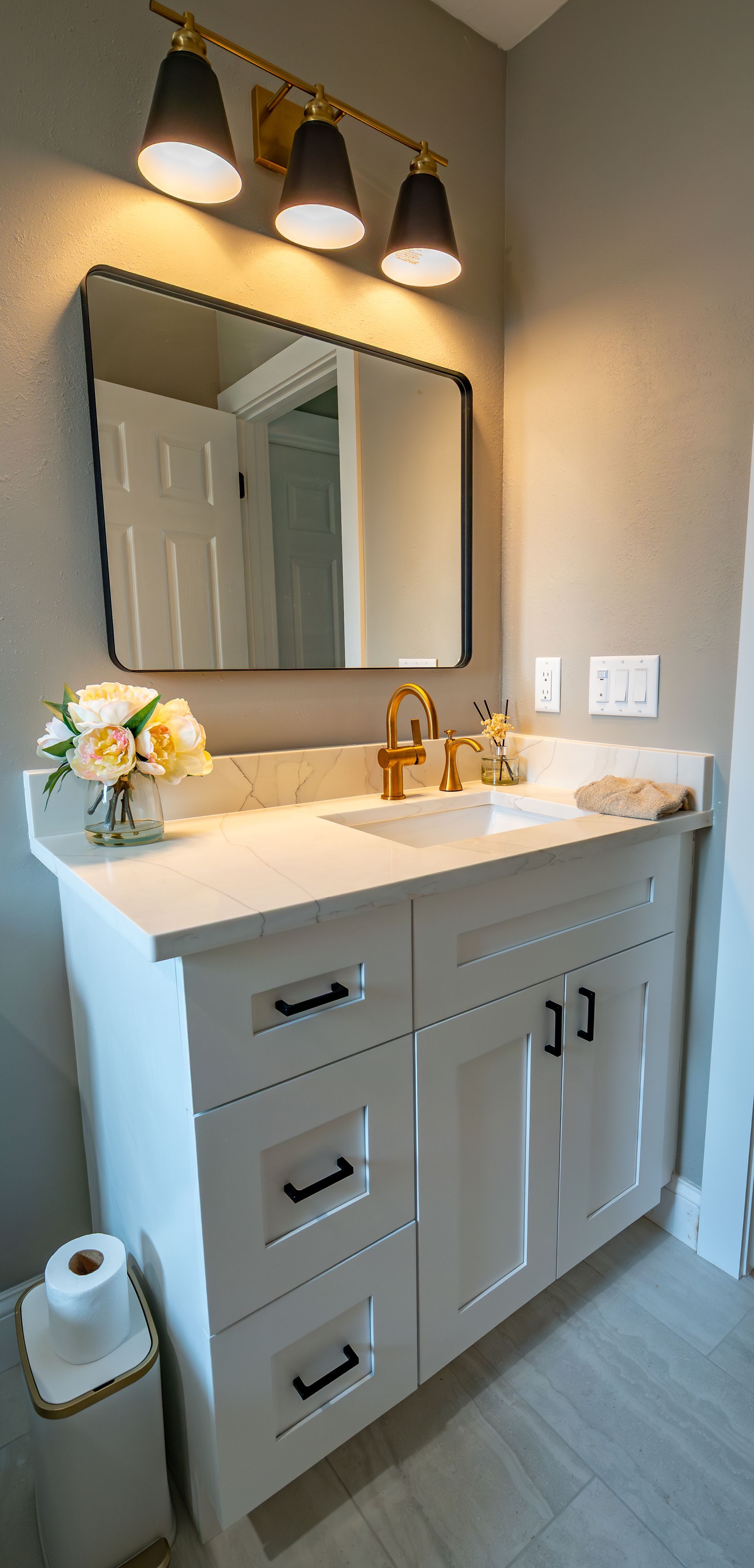 Bathroom vanity with white cabinets, black hardware, and gold accents.