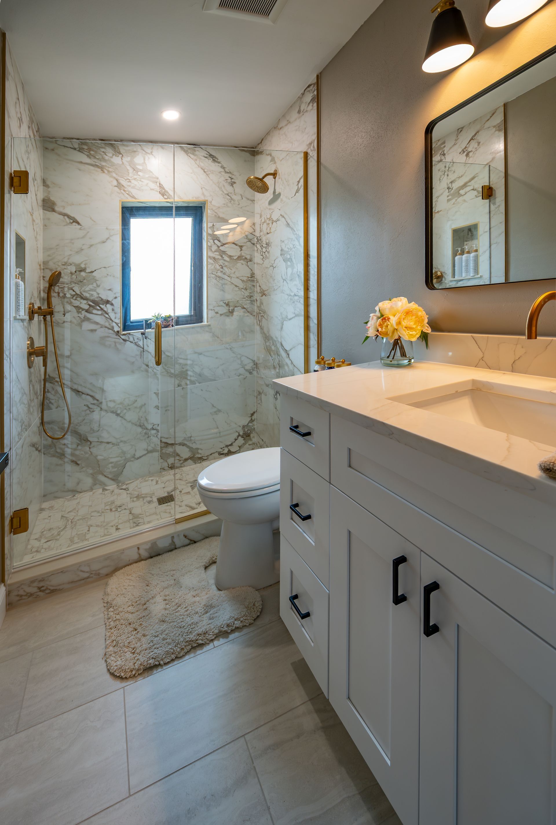 Bathroom with marble shower, white vanity, black hardware, gold fixtures.