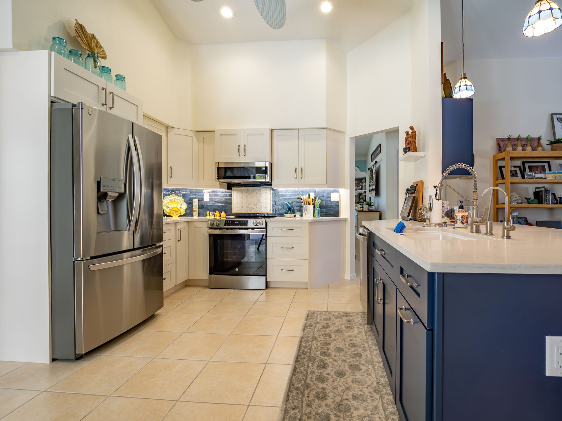 Modern kitchen with stainless steel appliances, blue island, light cabinets, and tile floor.