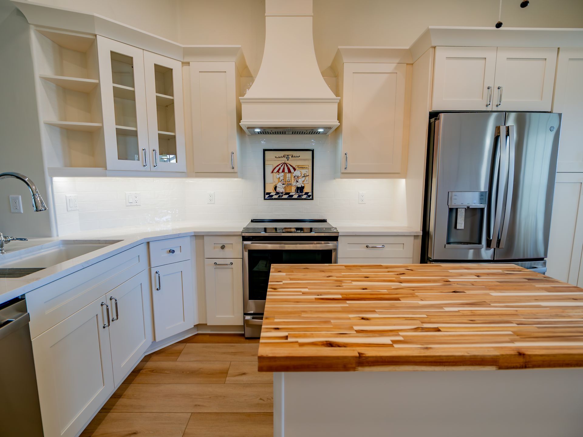 White kitchen with a wood countertop island, stainless steel appliances, and light wood floors.