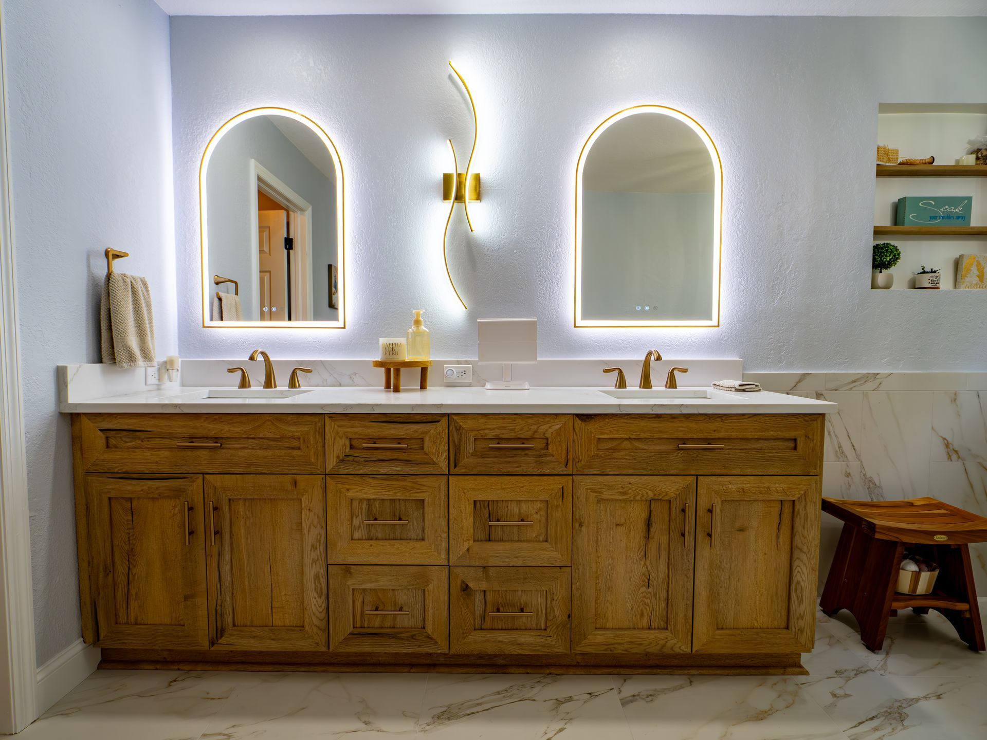 Bathroom with wooden vanity, arched mirrors, and gold fixtures.