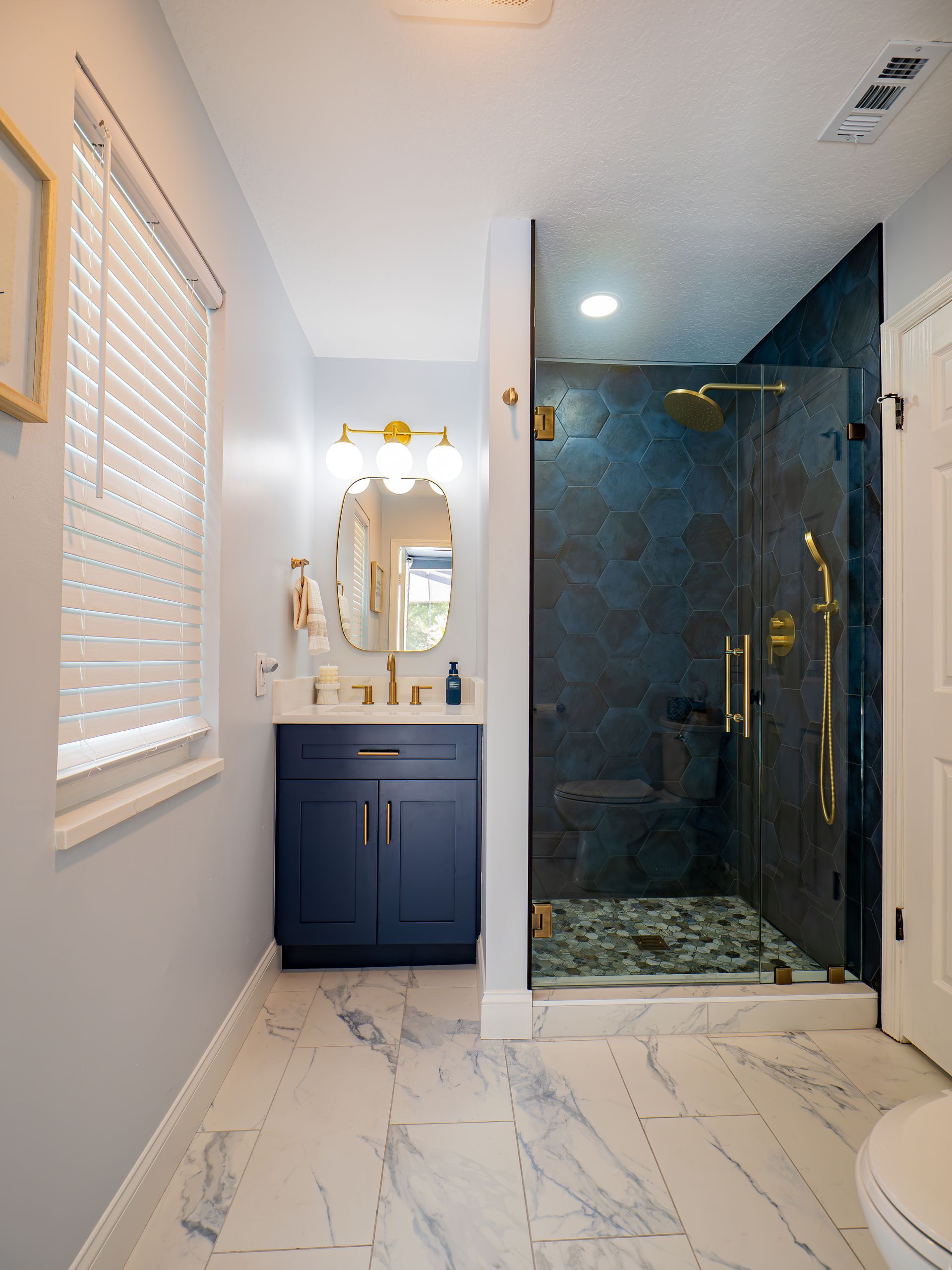 Blue and gold bathroom with shower, vanity, and marble flooring.