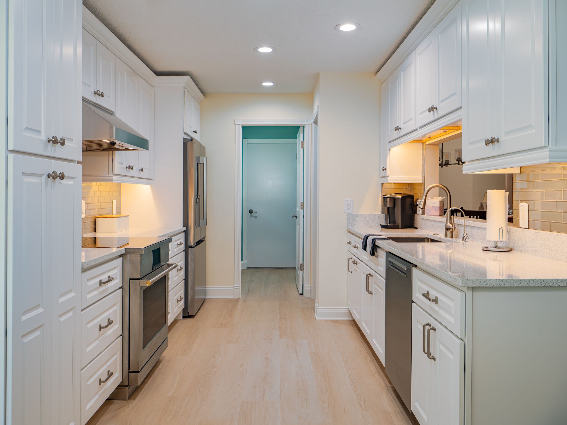 White kitchen with stainless steel appliances, light wood floor, and door in the background.